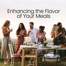 Five people stand by an outdoor dining table, smiling and talking while holding drinks, with a scenic landscape in the background. Text above reads, Enhance the Flavor of Your Meals with The Spice Lab Organic Starter Spice Set—18 USDA Certified Organic Jars.