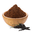 A Rico Rico Pasilla Chile Powder Shaker sits alongside a few dried black Pasilla chiles on a white background—an essential ingredient from Rico Rico for authentic Mexican cuisine.