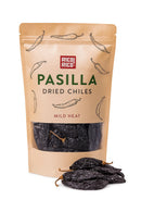 A brown pouch labeled Rico Rico Pasilla Dried Chiles – Mild & Rich Mexican Chile Negro from Oaxaca, featuring authentic chiles from the Rico Rico brand, with three whole dried chiles in front—ideal for adding rich depth to your mole negro.