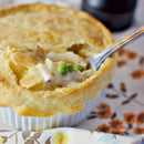A golden, flaky pot pie in a white ramekin is filled with creamy peas and potatoes, all seasoned with SALTOPIA Infused Sea Salts' BUMPIN' CHICKEN & DUMPLINS Chicken and Herbs Seasoning. The dish sits on a floral-patterned cloth.