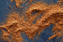 World Spice Poudre Douce by World Spice, a loose and aromatic sweet powder inspired by medieval spice blends, is scattered across a dark, textured surface, forming irregular patterns and small clumps throughout the image.