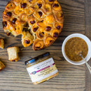 A round pull-apart bread with melted cheese and small sausages is served with a jar of Terrapin Ridge Farms Raspberry Honey Mustard Quart, the perfect gourmet condiment, plus a bowl of mustard and spoon on a wooden table.