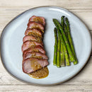 Sliced roast meat with Terrapin Ridge Farms Raspberry Honey Mustard Pretzel Dip arranged beside cooked asparagus on a light blue plate atop a wooden table.