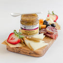 A wooden charcuterie board with cheese, salami, crackers, strawberries, blueberries, almonds, and a jar of Terrapin Ridge Farms Raspberry Honey Mustard Pretzel Dip (4.5 oz), topped with a white spoon.