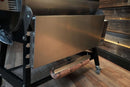 Pimp My Grill Tactical Stainless Folding Front Shelf for Recteq RT-700 / RT-680 attached to a grill, featuring a stainless steel folding shelf with a paper towel holder and a suspended roll of butcher paper for added prep space.