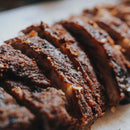 Close-up of sliced, seasoned, and grilled meat arranged in a row on a white surface. The edges are crispy and browned, revealing a juicy, tender interior—perfectly elevated with the Dead Rooster Co. Variety Pack - 3 Signature BBQ Rubs Bundle & Save by Dead Rooster Co.