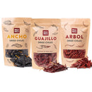 Three standing pouches of Rico Rico Dried Mexican Chiles 3-Pack – Ancho, Guajillo & Arbol Peppers display the visible dried chiles inside or beside each bag. Each pouch features vibrant chili illustrations and the Rico Rico brand name, making this a perfect gourmet spice kit for authentic Mexican flavors with ancho, guajillo, and arbol pepper varieties.