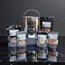 DDR BBQ Supply Manly Cans nut gift set featuring a metal bucket and five assorted snack pouches on a black surface.