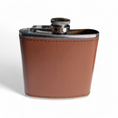 A stainless steel hip flask wrapped in brown leather stands upright on a white background—ideal paired with savory snacks from the Manly Cans 3.5 Gallon WeekCAN Warrior Gift Can.