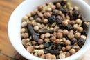 A white bowl filled with whole spices—such as coriander seeds, black peppercorns, cloves, and fennel seeds from World Spice Roast Chai by World Spice—sits on a wooden surface, perfect for making authentic Chai Masala.