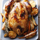 A golden-brown roasted chicken seasoned with SALTOPIA's BUMPIN' CHICKEN & DUMPLINS infused sea salt, garnished with rosemary, and served with roasted potato wedges, carrots, and lemon slices on a rectangular platter.