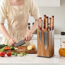 A person wearing a beige apron chops vegetables on a wooden board in the kitchen, with the Norpro Rotating Magnetic Knife Holder featuring an acacia wood block holding several knives on the countertop nearby.