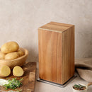 A tall, rectangular Norpro Rotating Magnetic Knife Holder with Acacia Wood Block sits on a metal base beside a wooden bowl of potatoes and a cutting board with sliced potatoes, set against a neutral background.