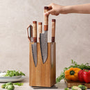 A hand lifts a knife from the Norpro Rotating Magnetic Knife Holder with Acacia Wood Block, elegantly displayed on the kitchen counter and surrounded by fresh vegetables including bell peppers, lettuce, and Brussels sprouts.