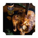A roasted whole chicken with crispy skin is served on a dark platter, garnished with herbs. A knife is inserted into the chicken, and a jar of Rufus Teague Chick N' Rub by Rufus Teague is visible in the background.