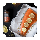 A raw salmon fillet with lemon slices and thyme sits on a tray alongside Rufus Teague Fish Rub, a gluten-free blend by Rufus Teague. Loose lemon slices and thyme sprigs are scattered nearby.