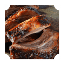 Close-up of juicy, grilled barbecue ribs with a caramelized glaze, sliced and stacked on a wooden surface. The tender meat has a crispy, flavorful crust thanks to Rufus Teague Meat Rub by Rufus Teague.