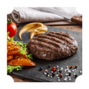 A grilled beef patty infused with Rufus Teague Smoke In a Bottle Liquid Smoke is served on a black slate plate with grilled tomato, lettuce, mustard, and mixed peppercorns. A whole tomato and folded napkin appear in the background.