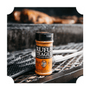 A bottle of Rufus Teague Spicy Meat Rub sits on a grill, its label visible, promising bold barbecue seasoning from Rufus Teague—perfect for adding flavor to your outdoor cooking or barbecuing.