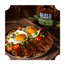 Grilled steak slices topped with Rufus Teague Steak Sauce, served with two sunny-side-up eggs, cherry tomatoes, and chopped green onions. A bottle of Rufus Teague Steak Sauce appears in the background.