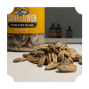 A close-up of Rufus Teague Sunflower Seeds piled in front of a yellow Sunflower Pitmaster Blend container from the Rufus Teague Sunflower Seeds Variety Pack. Bottles in the blurred background highlight its bold BBQ flavor.