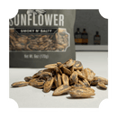 A close-up of roasted sunflower seeds piled on a white surface, with a Rufus Teague Sunflower Seeds Variety Pack bag blurred in the background. The image has rounded corners and highlights their bold BBQ flavor.