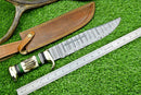 A Texan Knives Deluxe Dundee Knife, 16" handmade Damascus steel blade with brass guard and pakkawood or stag horn handle, lies by its leather sheath and a ruler showing it's about 32 cm, all on green artificial grass.