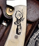 Close-up of the Texan Knives Custom Handmade J2 Steel Skinning Knife, featuring a 4.5" blade and an engraved camel bone handle with a stag's head design and two rivets, shown resting on brown leather.