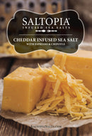 Blocks and shreds of cheddar cheese on wax paper with a grater. Text: “SALTOPIA Infused Sea Salts: Cheese Salt – CHEDDAR CHEESE. Explore this bold cheddar seasoning at SaltopiaSalts.com.”.
