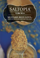 A spoonful of grainy mustard hovers above an open jar, with SALTOPIA Infused Sea Salts' French Mustard Salt: MUSTARD BEEN LOVE text over a blue background.
