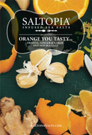 A product label for SALTOPIA Infused Sea Salts’ Orange & Garlic Salt: ORANGE YOU TASTY, featuring orange slices, ginger root, garlic cloves, and orange peels on a dark green background—a vibrant citrus garlic seasoning.