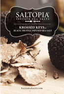 Close-up of black truffles and shavings on wood. Label reads SALTOPIA Infused Sea Salts, KROSSED KEYS Black Truffle Salt, made with Black Italian Truffles. Website SaltopiaSalts.com appears at the bottom.