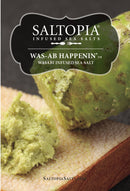 A close-up of SALTOPIA Infused Sea Salts’ Saltopia Wasabi Salt: WAS-AB-HAPPENIN, perfect for sushi, with wasabi-infused sea salt on bread. Text describes it as WAS-AB HAPPENIN wasabi infused sea salt.