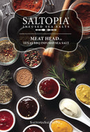 An assortment of spices, seasonings, and sauces is displayed on a dark surface with jars and bowls, highlighting SALTOPIA Infused Sea Salts’ BBQ Salt: MEAT HEAD seasoning at the center.