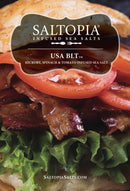 Close-up of a BLT sandwich topped with SALTOPIA Infused Sea Salts' BLT Salt: BACON. LETTUCE. TOMATO., featuring hickory-smoked sea salt. Overlay text: SaltopiaSalts.com.