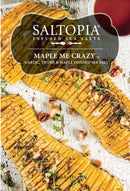 Three sliced and roasted sweet potatoes are topped with herbs and chopped nuts, displayed on a rustic white wood surface. A small dish of brown liquid sits nearby. The image showcases SALTOPIA Infused Sea Salts' Maple Garlic & Thyme Salt: MAPLE ME CRAZY.