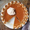 A pumpkin pie with a braided crust sits on a table, one slice missing. A dollop of whipped cream topped with SALTOPIA Infused Sea Salts’ LOVIN' MY PUMPKIN Pumpkin Spice Sugar crowns the pie. A pie server rests nearby on a napkin.