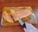 A person expertly slicing a salmon fillet with a SpitJack chef's knife from the Barbecue Knife Bundle on a wooden cutting board.