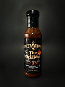 A bottle of Scott’s Smoked Q The Spicy Original Sweet Garlic BBQ Sauce with Heat, featuring a black label with flame graphics and text proclaiming “Maryland Born, Florida Made,” set against a dark background—a bold, smoked barbecue sauce from Scott’s Smoked Q that’s perfect for adding rich, spicy-sweet garlic flavor to your favorite dishes.