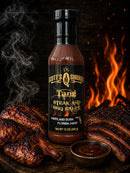 A bottle of Scott’s Smoked Q Tang North Carolina-Style Vinegar BBQ Sauce—crafted by Scott’s Smoked Q in the tradition of authentic North Carolina barbecue—is set beside grilled steak, a small bowl of savory finishing sauce, and a flaming grill in the background. Steam curls up from the meat amidst a dark, rustic atmosphere.