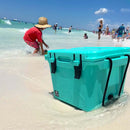 Seafoam colored 25 quart cooler by Bison Coolers on a sandy beach in shallow water with a braided rope handle.