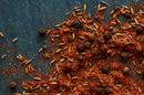 A close-up of World Spice Shawarma Spice by World Spice—featuring a vibrant medley of ground red powder, whole black peppercorns, and cumin seeds—scattered richly across a dark surface to capture the essence of Middle Eastern cuisine.