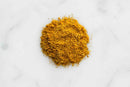 A small mound of World Spice Poudre de Colombo Curry, a key ingredient in French Caribbean curry, is spread on a white marble surface.