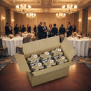 An open case of Texas Pecan Cake 30-Pack by Texas Pecan Cakes sits on a table in a banquet hall, with people in formal attire conversing in the blurred background and round tables set for an event dessert featuring these cakes.