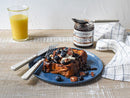 A plate of French toast topped with blueberries, pecans, cream, and chocolate sauce sits beside a glass of orange juice and Terrapin Ridge Blueberry Bourbon Pecan Jam by Terrapin Ridge Farms—an ideal choice for breakfast spreads.