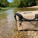 Sand soft-sided cooler bag by Bison Coolers, featuring black straps and a bottle opener keychain in an outdoor setting.