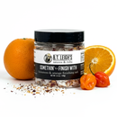 A jar of B.T. Leigh’s Habanero & Orange Finishing Salt surrounded by a whole orange, a sliced orange, and two habanero peppers.