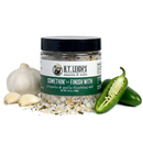 A jar of B.T. Leigh’s Jalapeno & Garlic Finishing Salt surrounded by fresh garlic cloves and halved jalapeños.