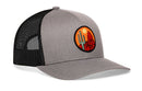 Introducing the Haka Hat Southwest Sunset Trucker Hat—a gray and black mesh snapback featuring a round embroidered patch with a green cactus, red mountains, and an orange sun, capturing true desert vibes from Haka Hat.