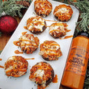 A platter of stuffed mushrooms with melted cheese and a smoky flavor from Terrapin Ridge Farms Spicy Chipotle Garnishing Squeeze 14 oz sits on a white tray, festive greenery, and a red ornament nearby. The bottle is beside the tray.